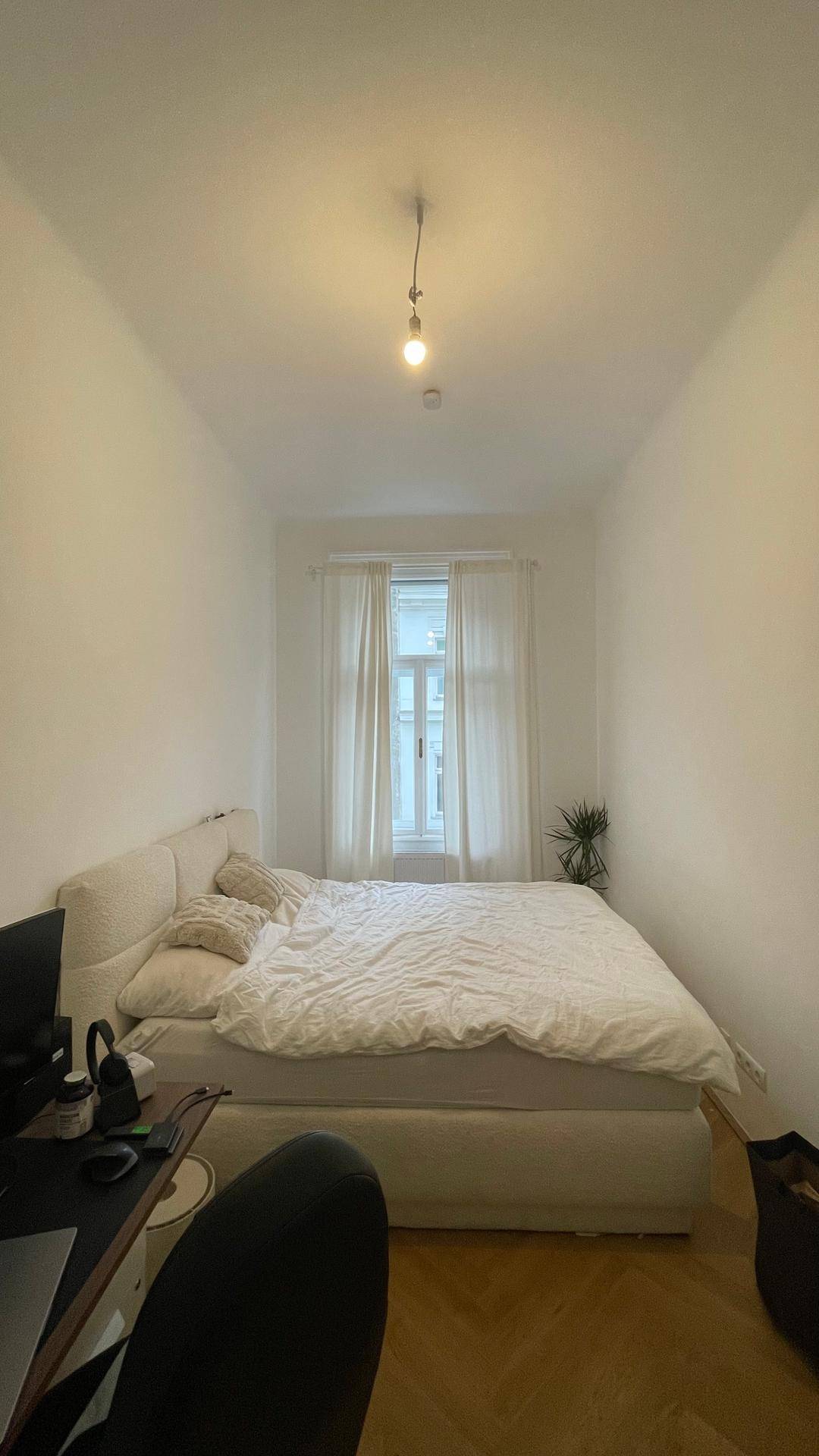 Gemütliches Schlafzimmer mit Doppelbett, Vorhängen und Fischgrätparkett.