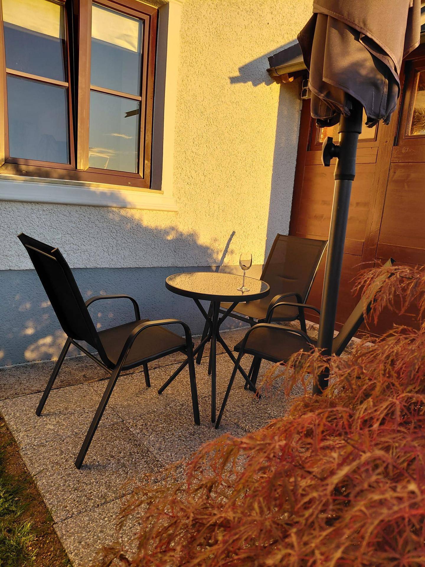 Gemütlicher Außenbereich mit Tisch und Stühlen unter einem Sonnenschirm, beleuchtet von der Abendsonne.