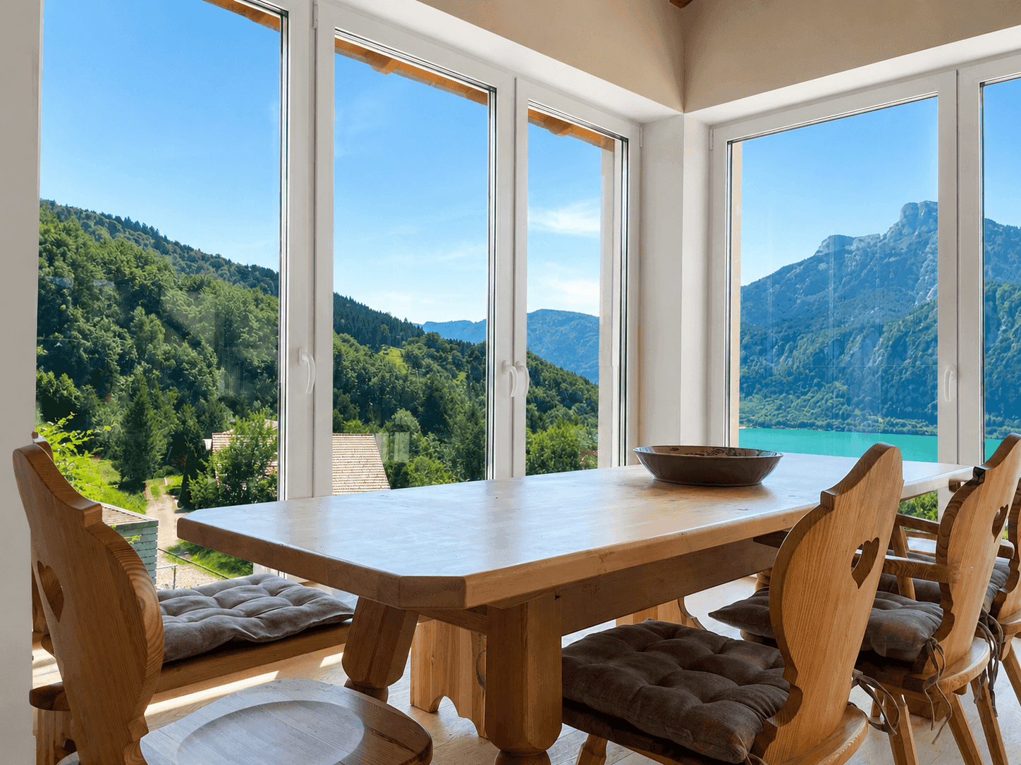 Essbereich mit rustikalem Holztisch und Bänken, umgeben von Fenstern mit Bergblick.