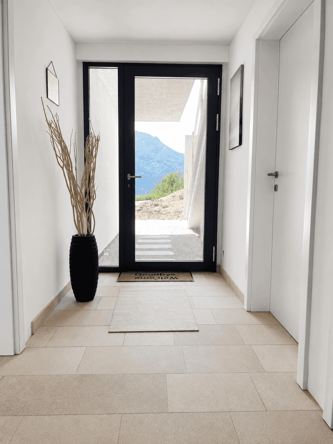 Heller Eingangsbereich mit Fliesenboden und Blick auf die Berge durch die Glastür.