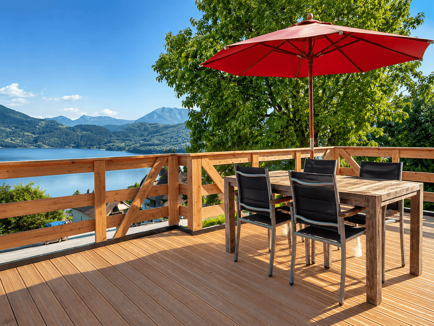 Große Holzterrasse mit Esstisch, Sonnenschirm und weitem Blick auf den See und die Berge.