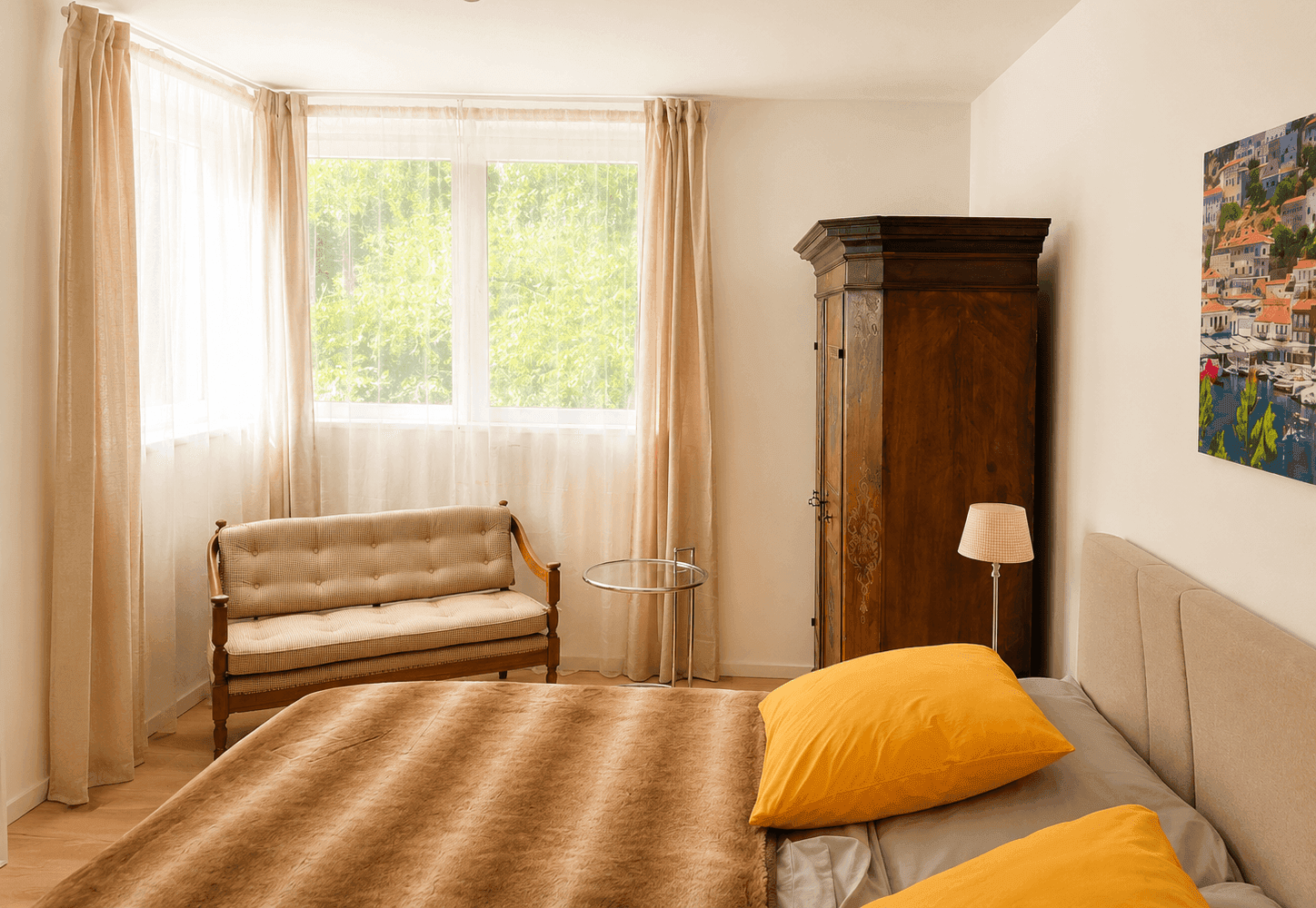Schlafzimmer mit großem Fenster, beigem Sofa und traditionellem Holzschrank.
