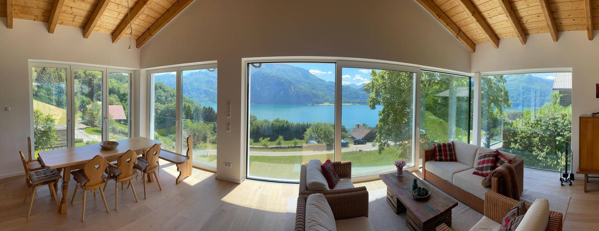 Großzügiger Wohn- und Essbereich mit Holzbalkendecke und Panoramafenstern mit Seeblick.