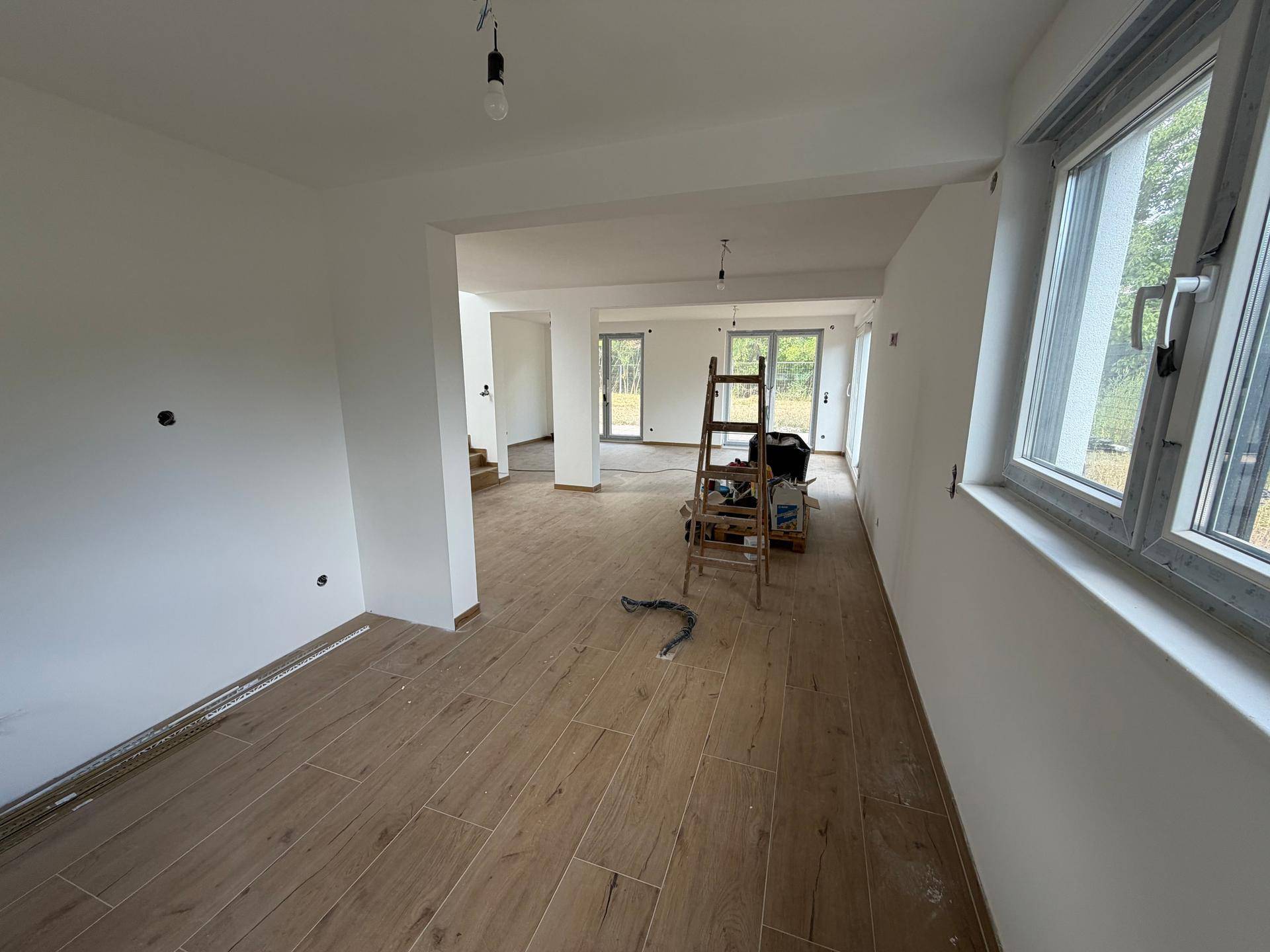 Weitläufiger, offener Wohnbereich im Rohbau mit großen Fenstern und Blick auf den Garten.