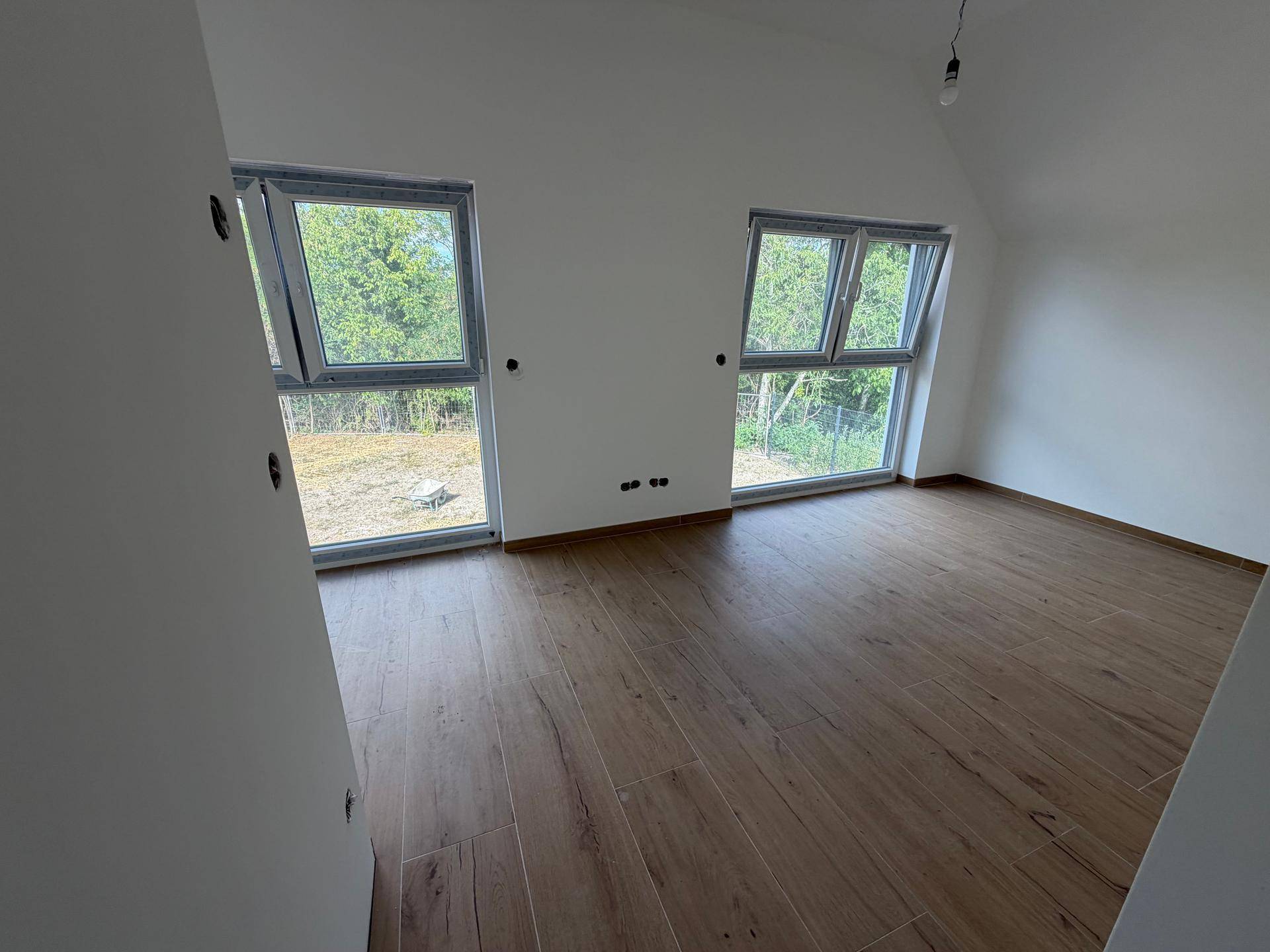 Geräumiges Zimmer mit zwei großen Fenstern, die viel Tageslicht hereinlassen und einen Blick ins Grüne bieten.