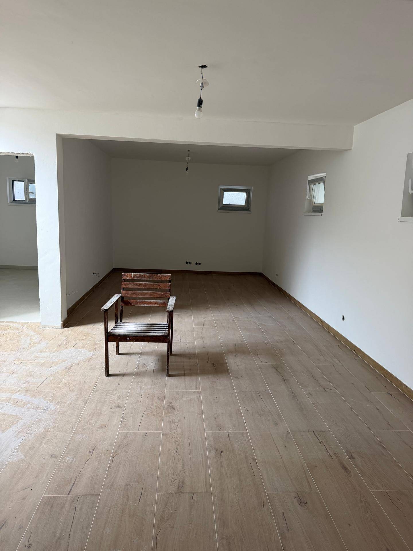 Weitläufiger Wohnbereich im Rohbau mit Fliesen in Holzoptik und einem einzelnen Holzstuhl.