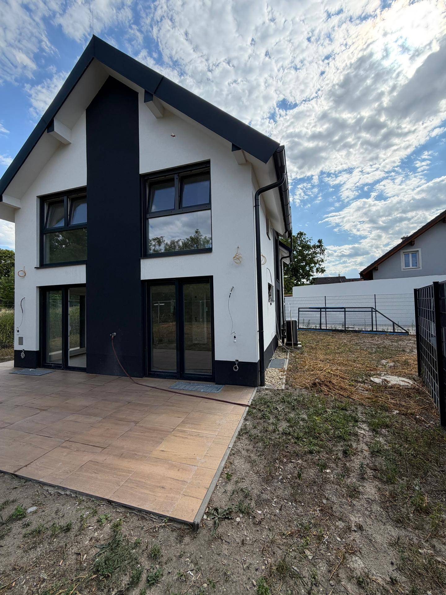 Rückseite des modernen Hauses mit großer gefliester Terrasse und Zugang zum Garten.