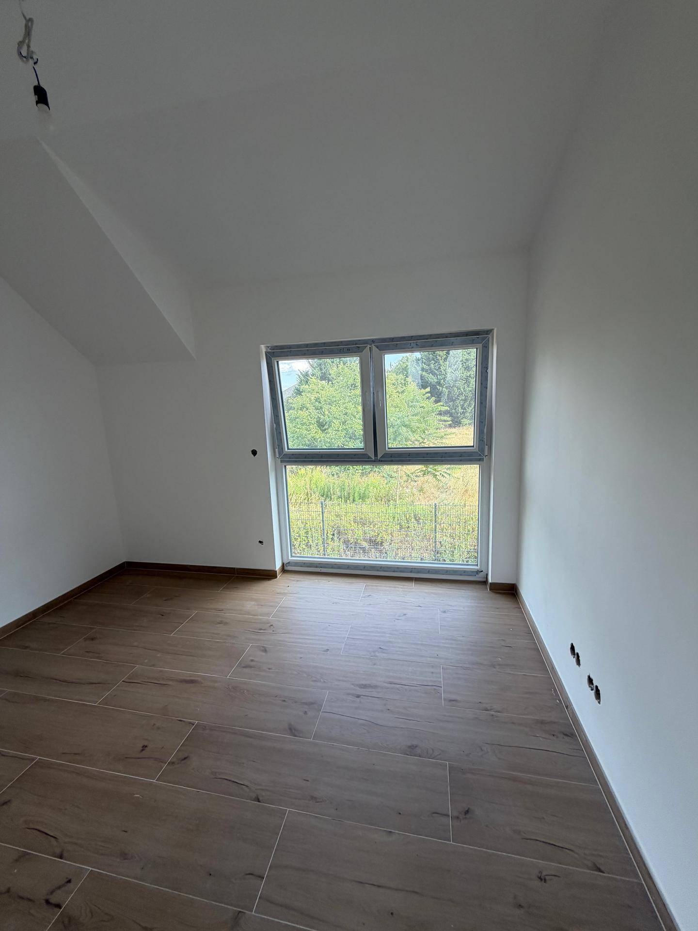 Helles Schlafzimmer im Dachgeschoss mit großen Fenstern und Blick ins Grüne, ausgestattet mit Fliesen in Holzoptik.