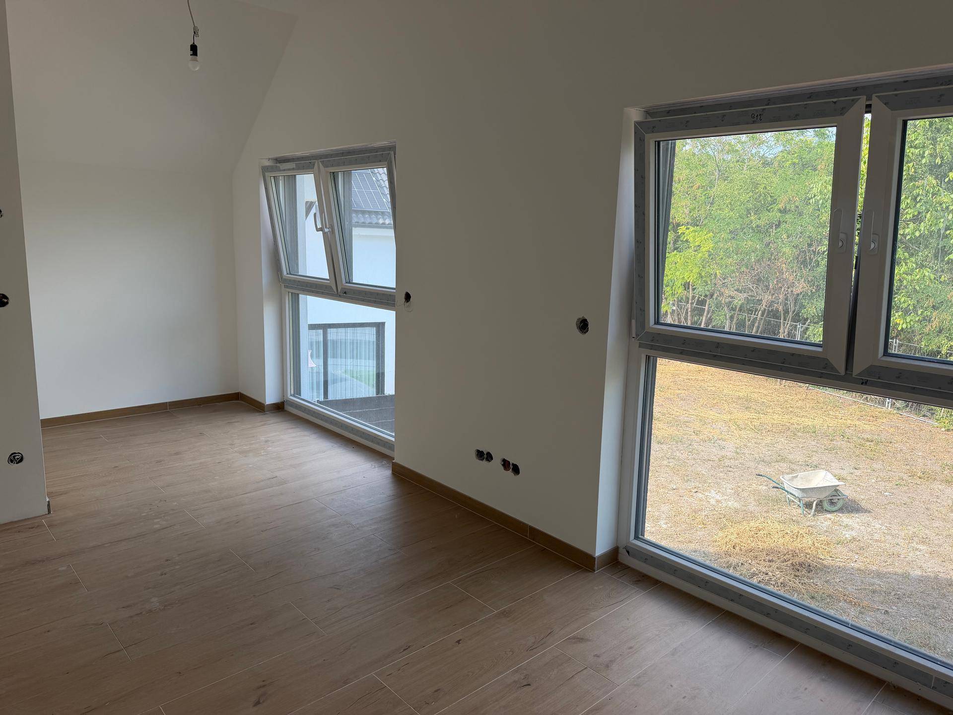 Helles Zimmer im Dachgeschoss mit großen Fenstern und Blick ins Grüne, ausgestattet mit Fliesen in Holzoptik.