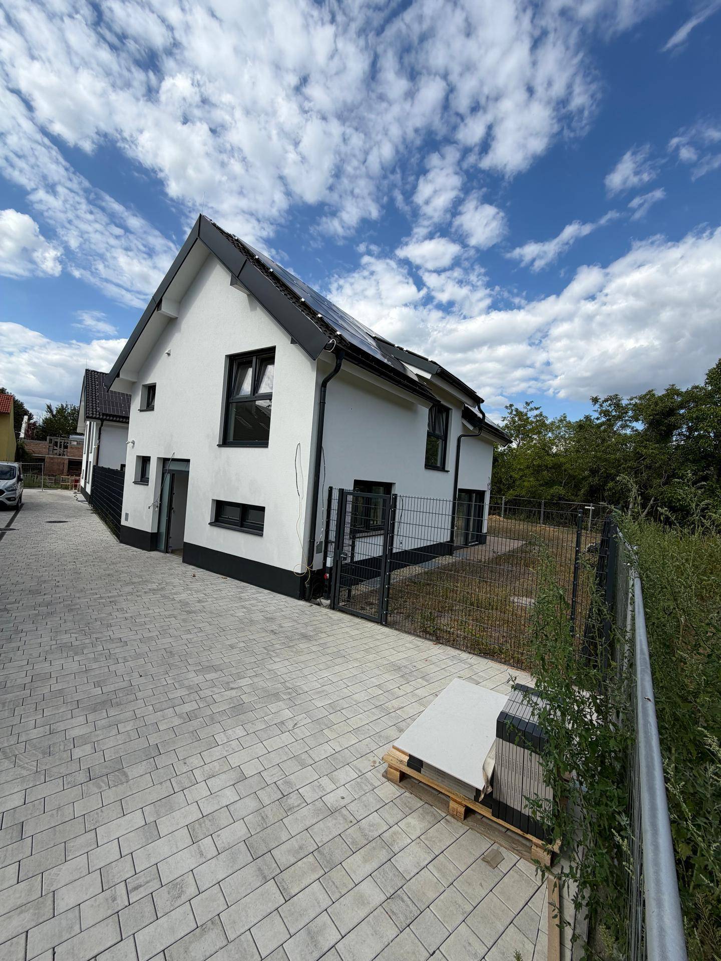 Modernes Einfamilienhaus mit weißer Fassade, dunklem Dach und gepflasterter Auffahrt.