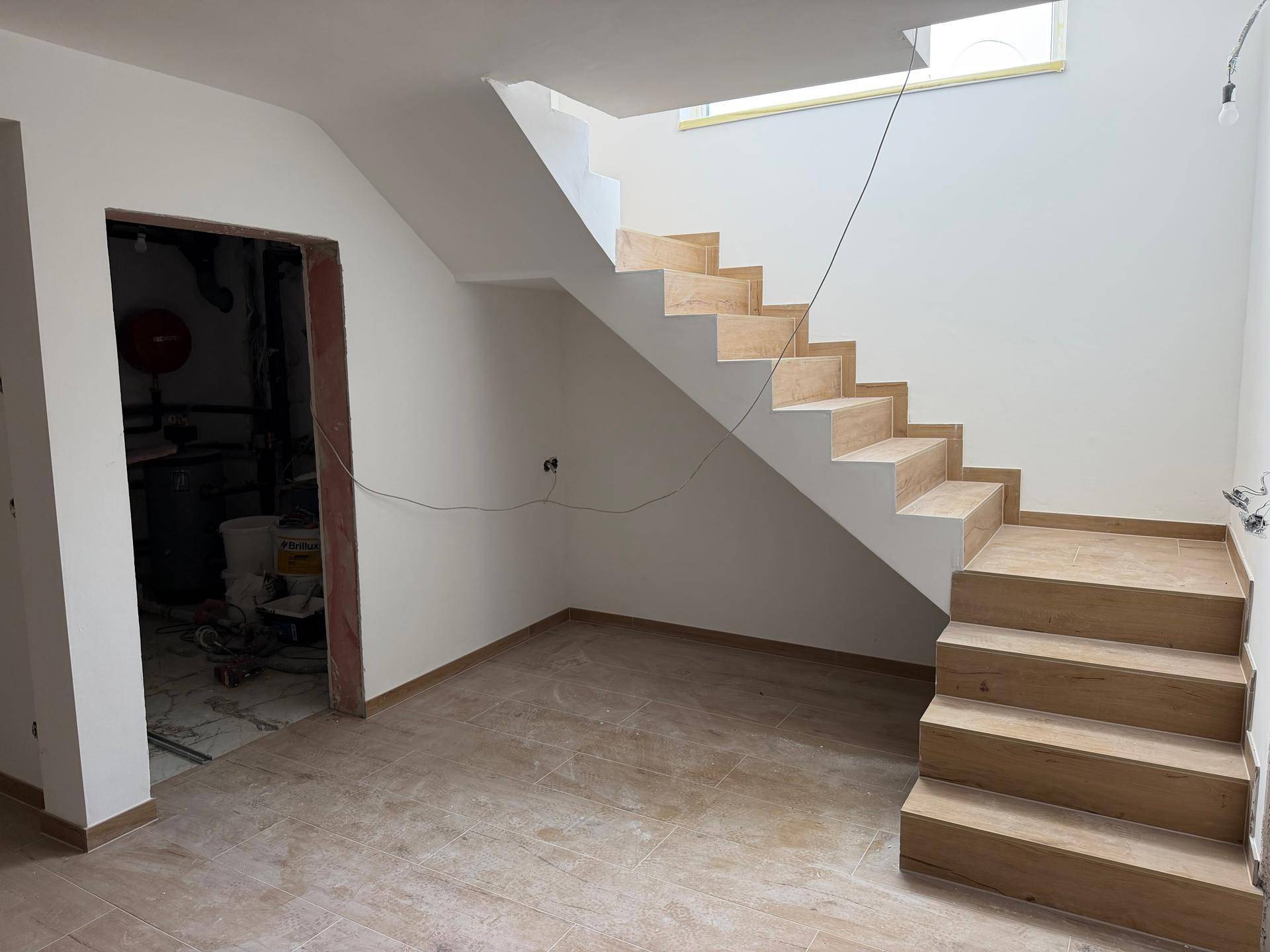 Heller Flurbereich mit moderner Holztreppe und Fliesen in Holzoptik, führt zu weiteren Räumen.