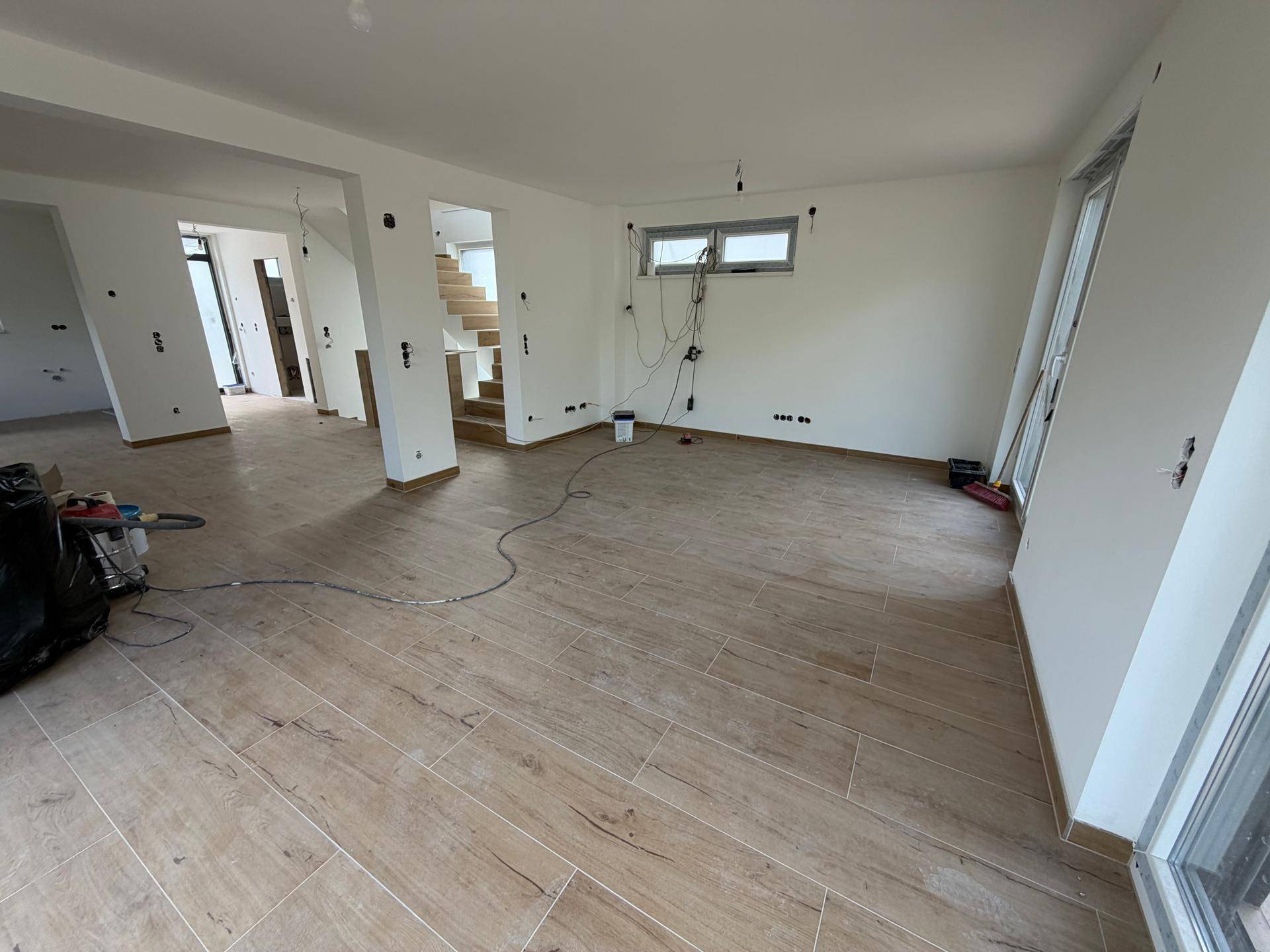 Großer, offener Wohnbereich im Rohbau mit Treppenzugang und viel Tageslicht durch die Fenster.