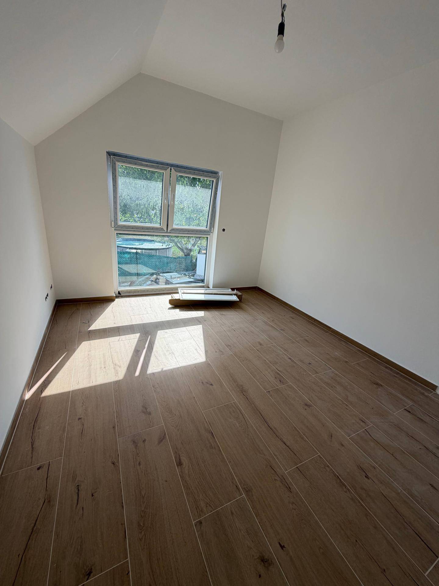 Helles Zimmer im Dachgeschoss mit Fliesen in Holzoptik und einem großen Fenster mit Blick auf den Garten.