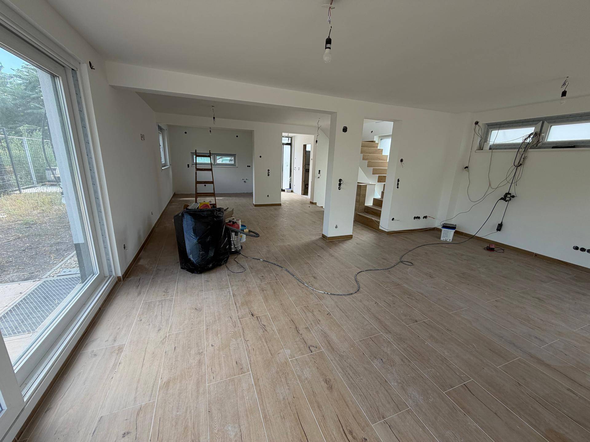 Großer, offener Wohn- und Essbereich im Rohbau mit großen Fenstern und Blick ins Grüne.