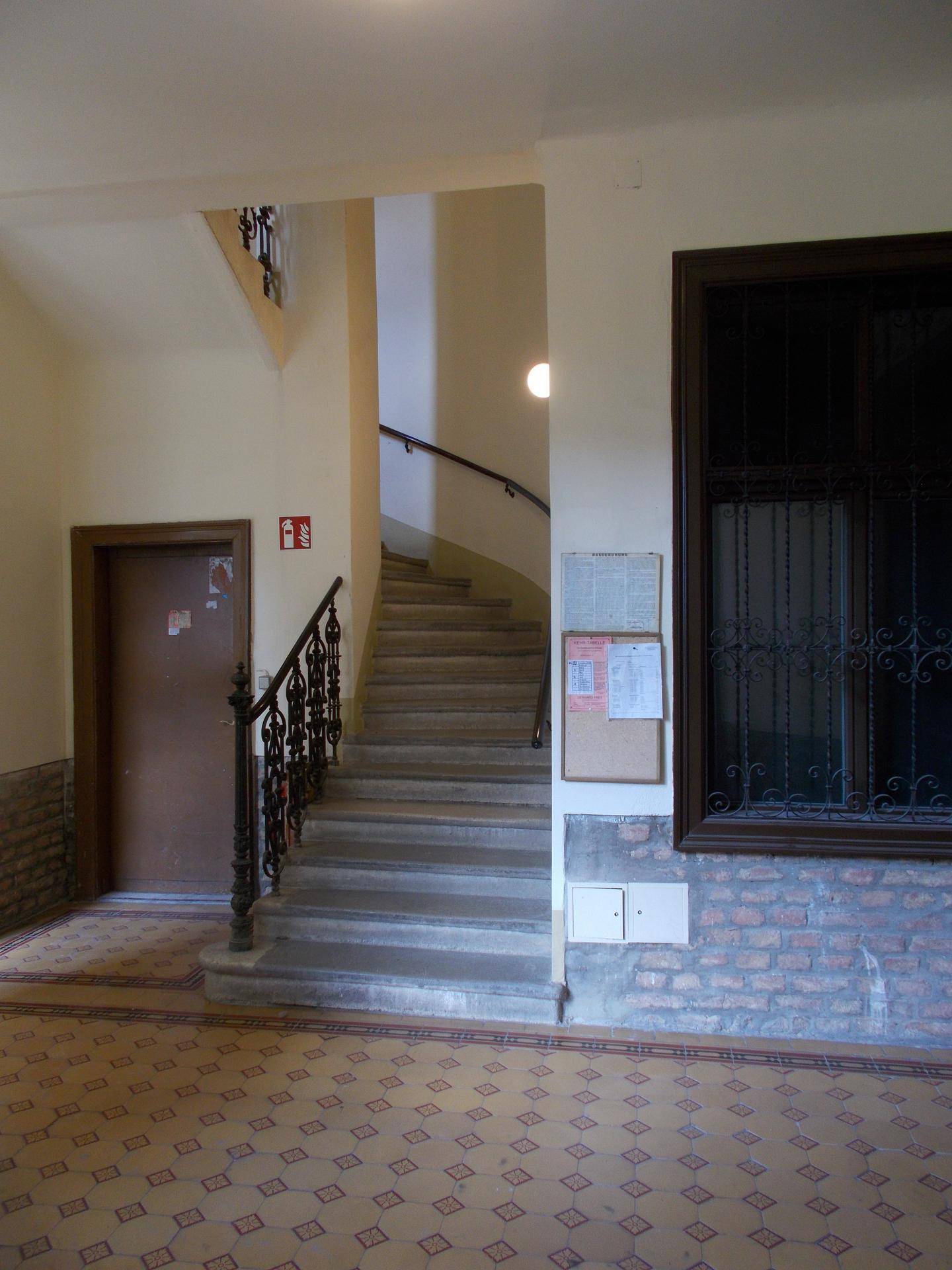 Treppenhaus in einem Altbau mit historischem Geländer und gemustertem Fliesenboden.