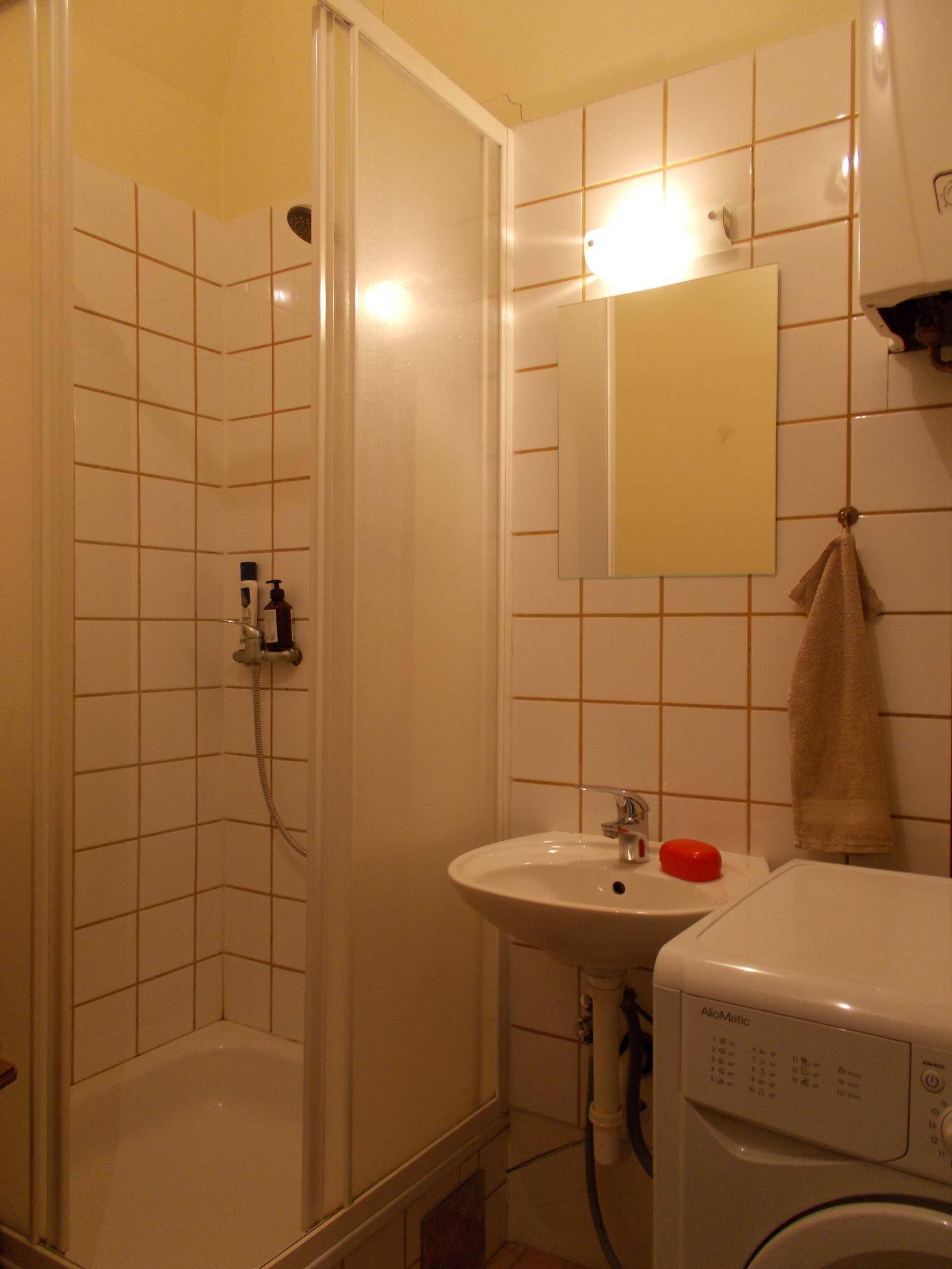 Kleines Badezimmer mit Duschkabine, Waschbecken und Waschmaschine, hell gefliest.