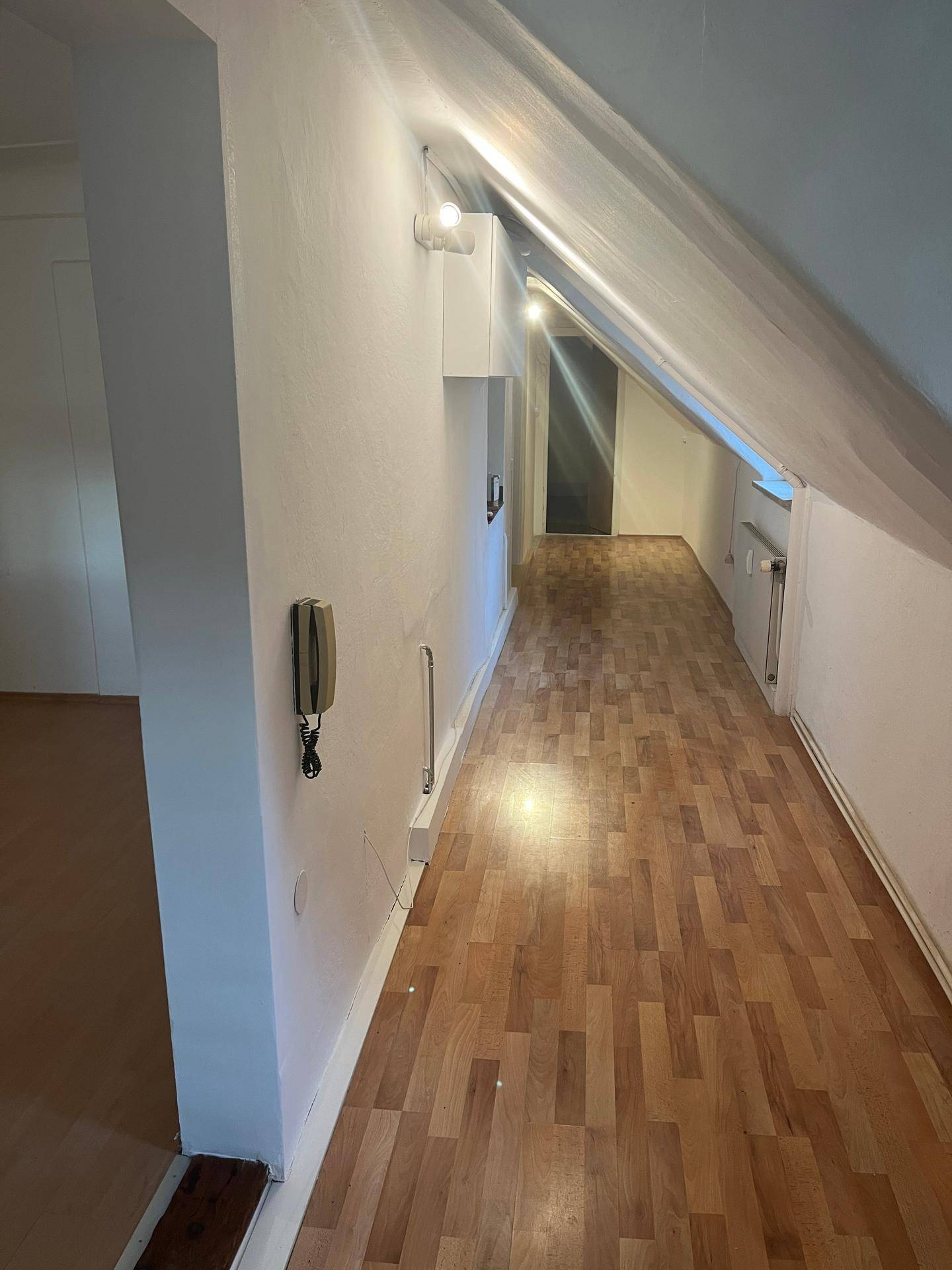 Langer Flur im Dachgeschoss mit schrägen Wänden, Holzfußboden und einer Gegensprechanlage an der Wand.