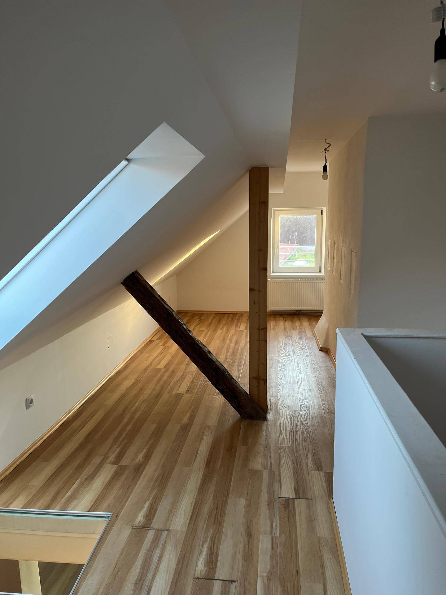 Geräumiger Dachgeschossflur mit schrägen Wänden, Holzbalken und einem Fenster am Ende, das Licht spendet.