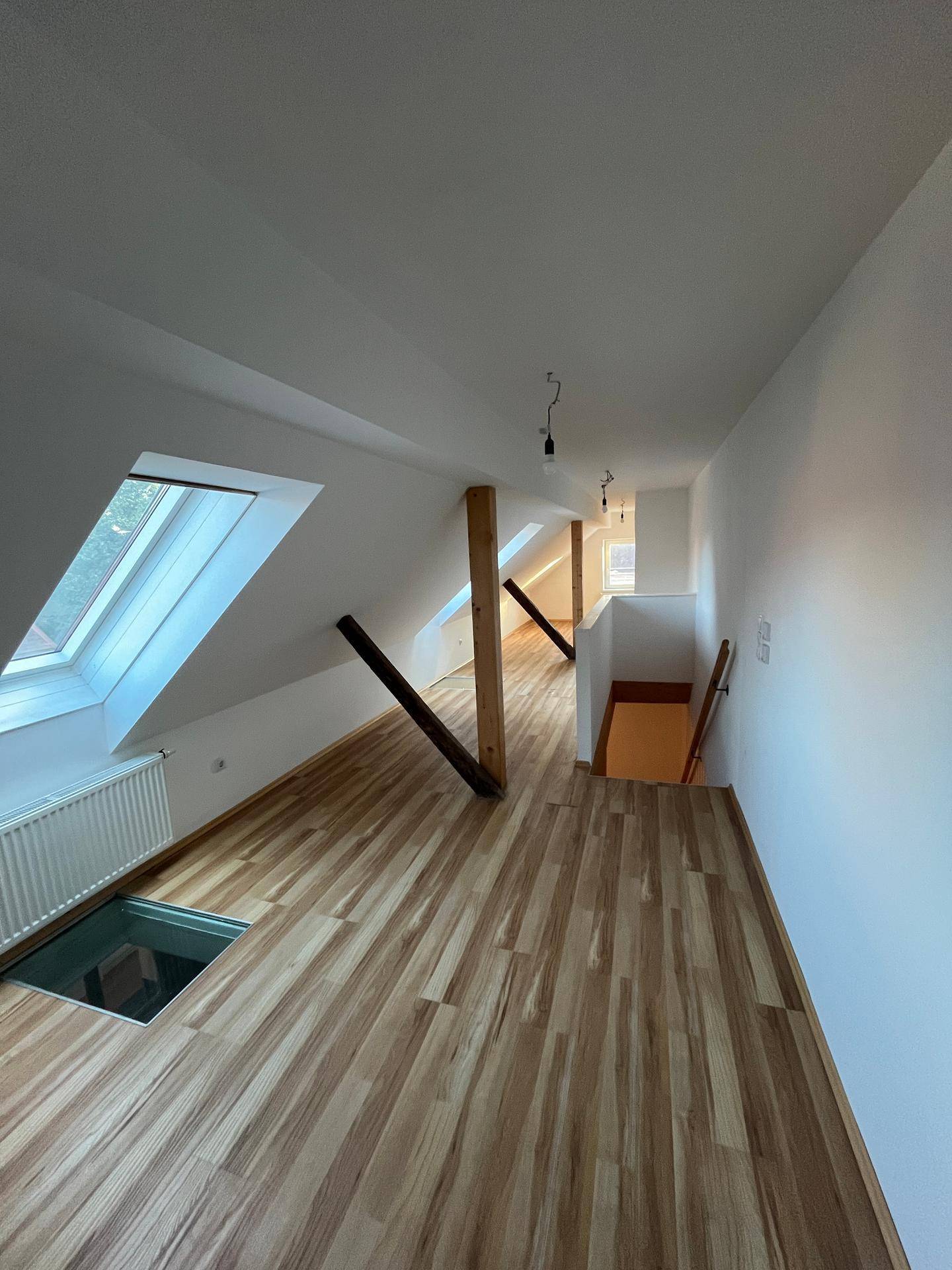 Heller Dachgeschossflur mit Laminatboden, sichtbaren Holzbalken, Dachfenstern und einem Glasboden-Element.