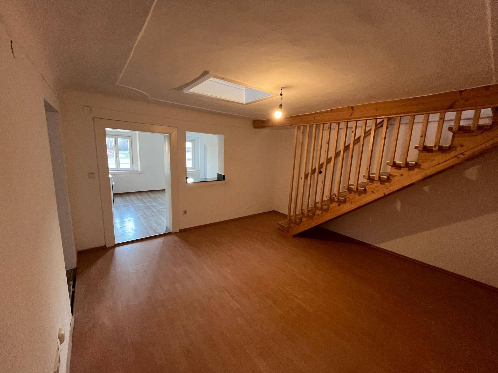 Heller Wohnbereich mit Holztreppe, Laminatboden und einem Dachfenster, das den Raum mit Licht erfüllt.
