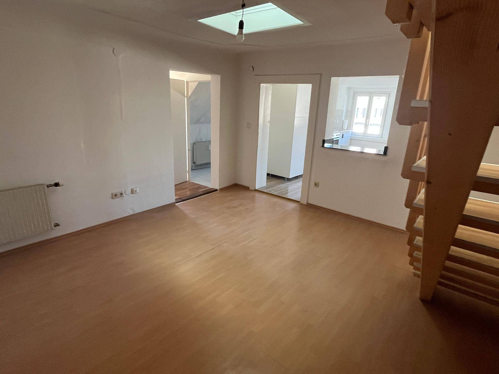 Offener Wohnbereich mit Holztreppe, Laminatboden und Dachfenster, das den Übergang zu angrenzenden Räumen betont.