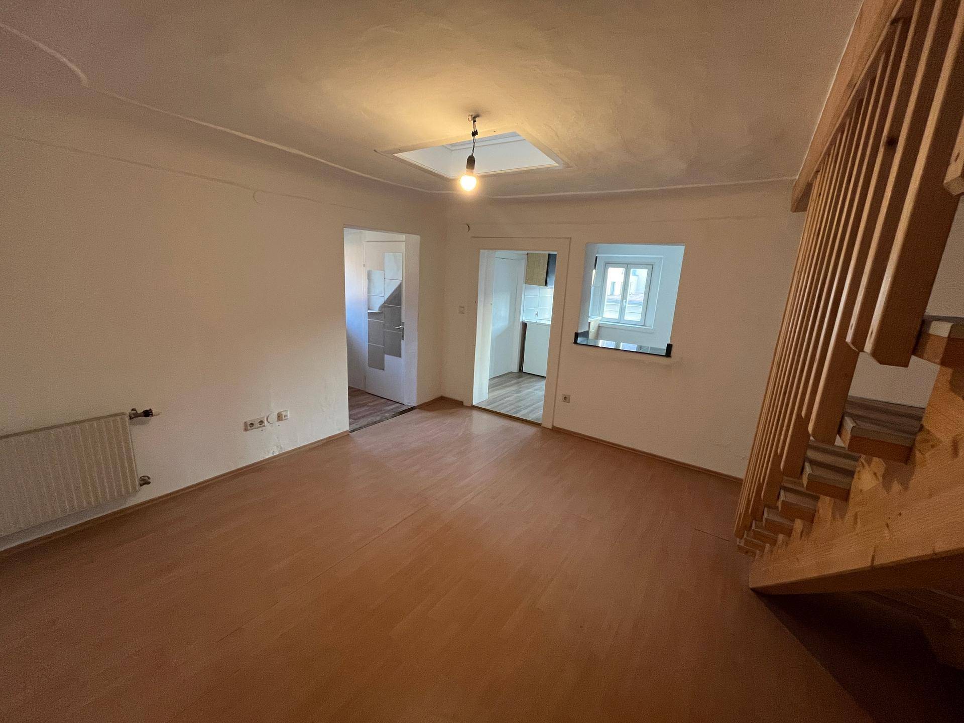 Geräumiger Wohnbereich mit Holztreppe, Laminatboden und einem Dachfenster, das für eine angenehme Atmosphäre sorgt.
