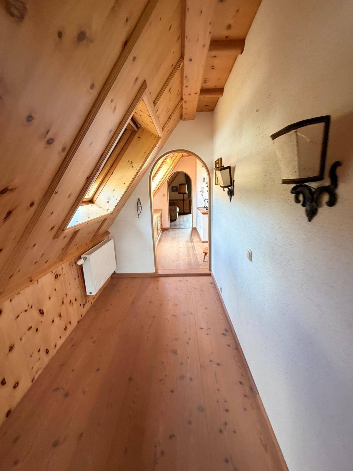Langer Flur im Dachgeschoss mit Holzboden, Holzvertäfelung und Rundbögen zu weiteren Räumen.