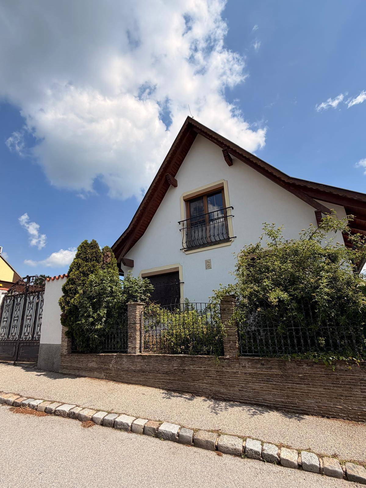 Charmantes Einfamilienhaus mit Satteldach, schmiedeeisernem Zaun und gepflegter Bepflanzung.