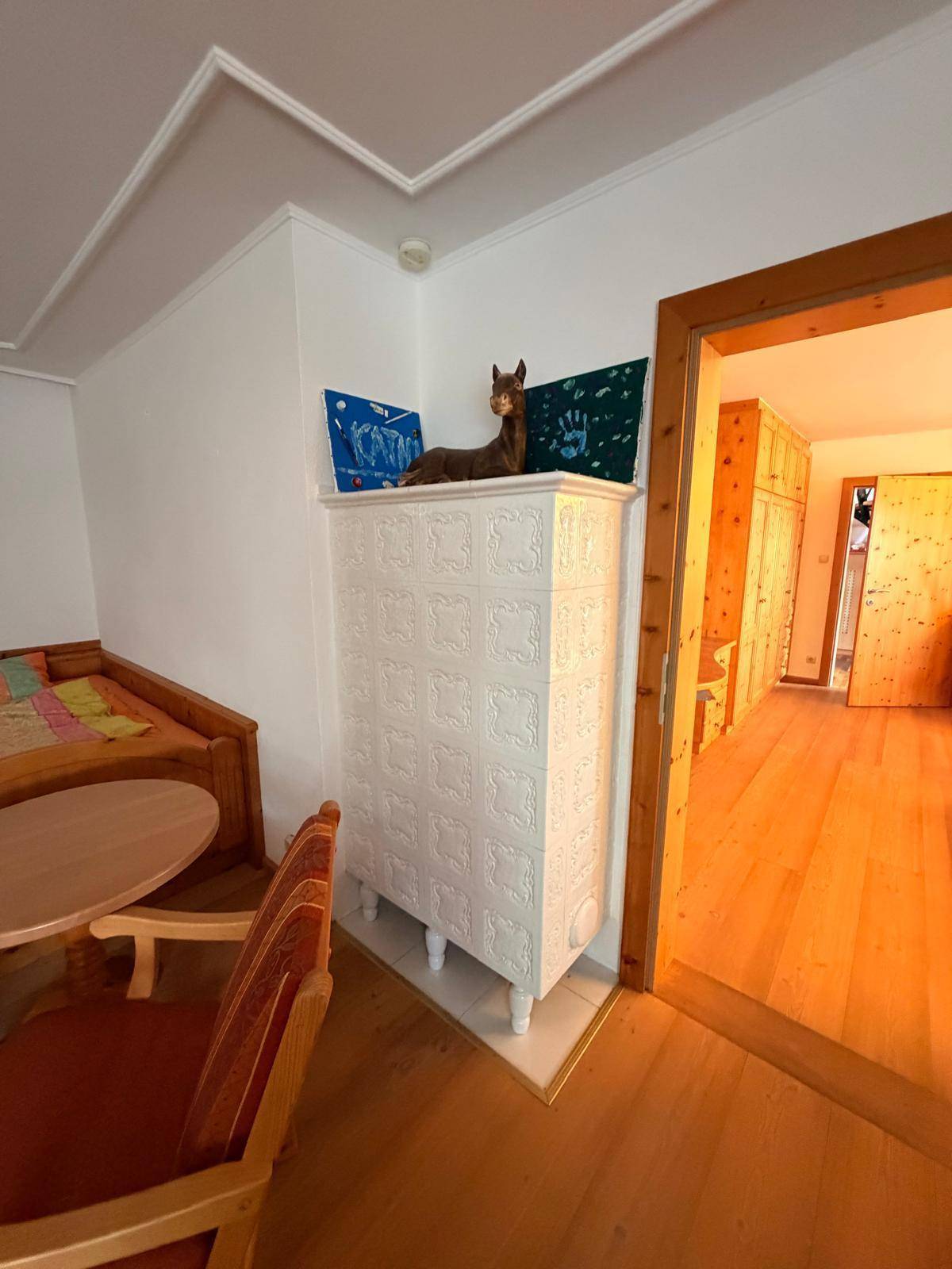 Gemütliches Zimmer mit weißem Kachelofen, Holzboden und traditionellen Möbeln.