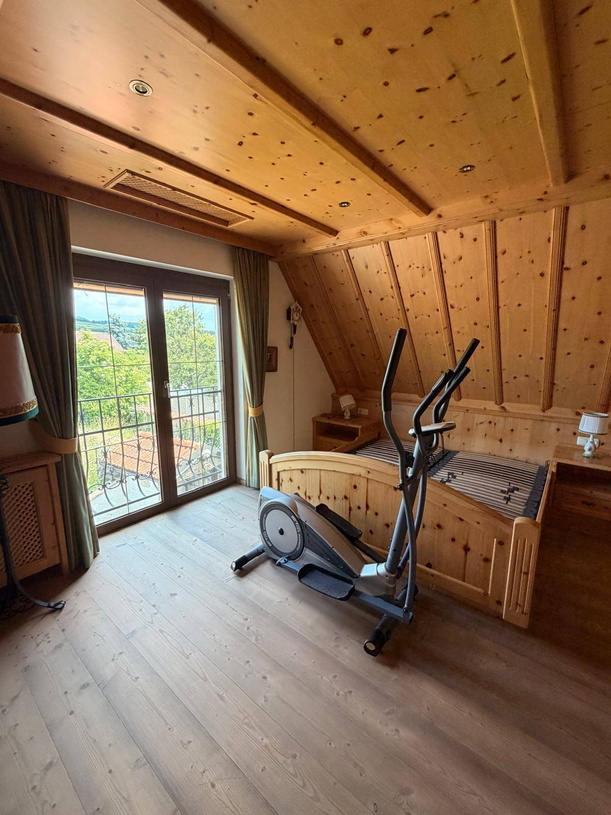 Schlafzimmer im Dachgeschoss mit Holzausstattung, Balkonzugang und Trainingsgerät.