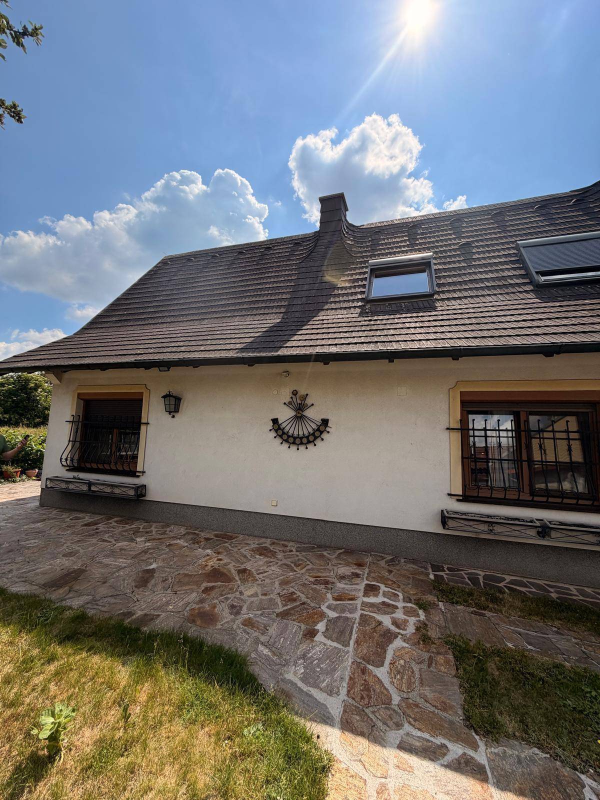 Seitenansicht des Hauses mit Satteldach, Dachfenstern und gepflastertem Bereich.