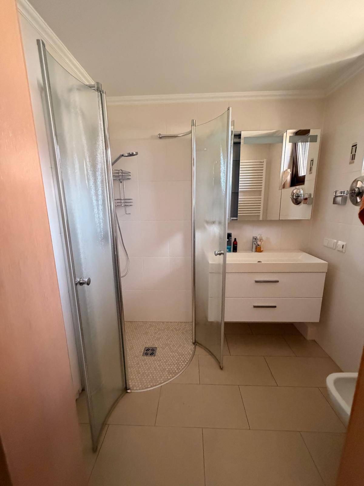 Helles Badezimmer mit Duschkabine, Fliesenboden und modernem Waschtisch mit Spiegelschrank.