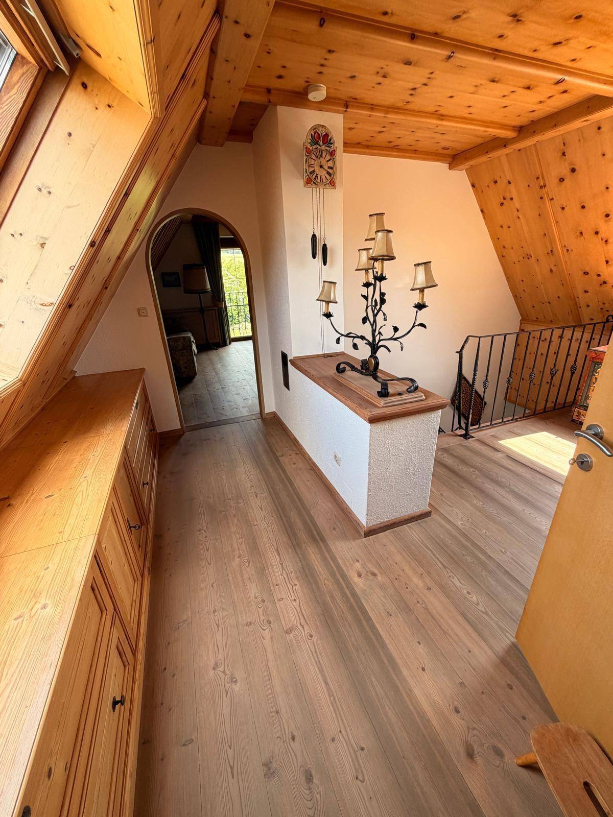 Heller Flur im Dachgeschoss mit Holzvertäfelung, dekorativer Leuchte und Blick in den Nebenraum.