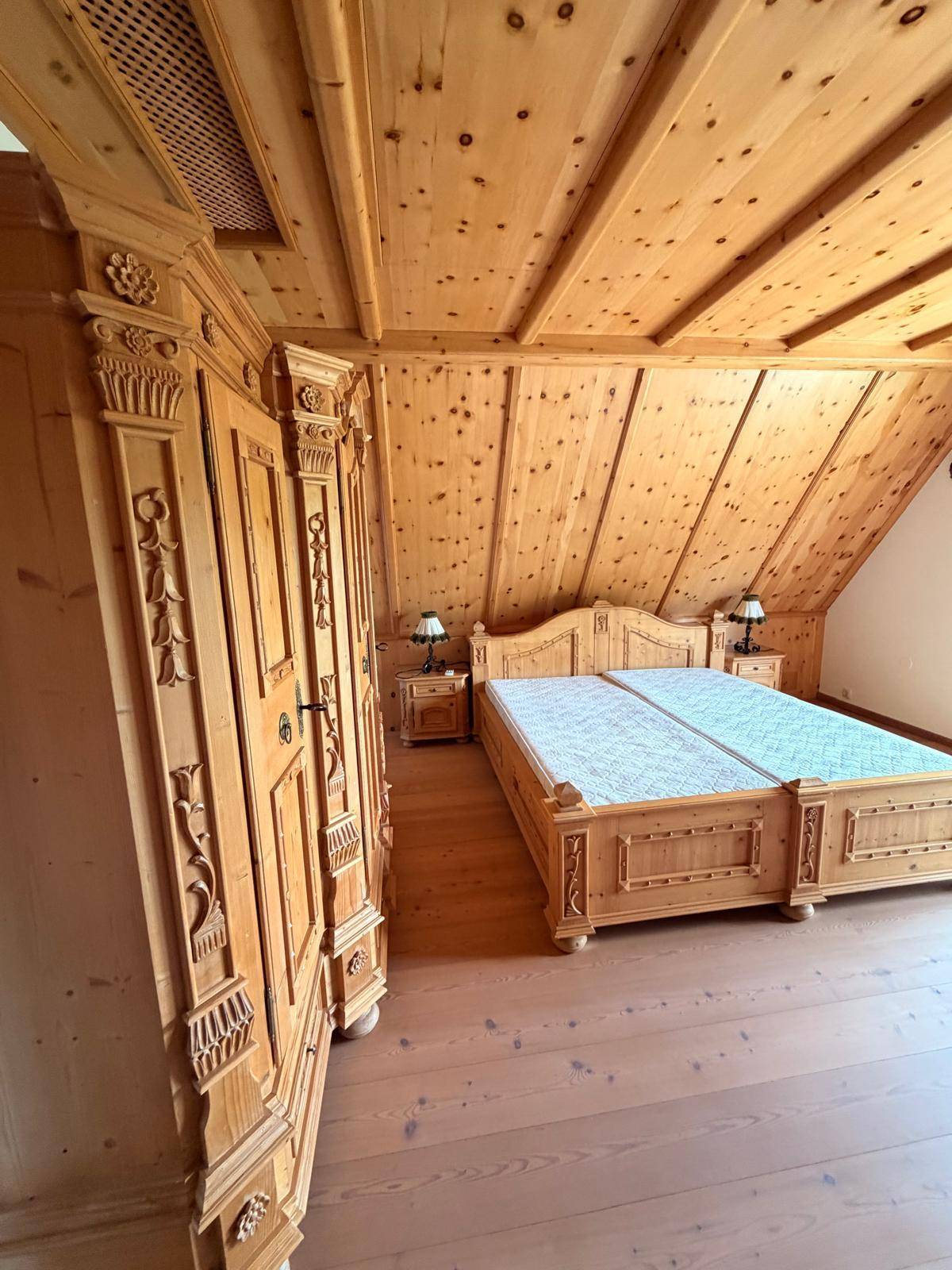 Traditionelles Schlafzimmer mit geschnitzten Holzmöbeln, Holzboden und holzvertäfelter Decke.