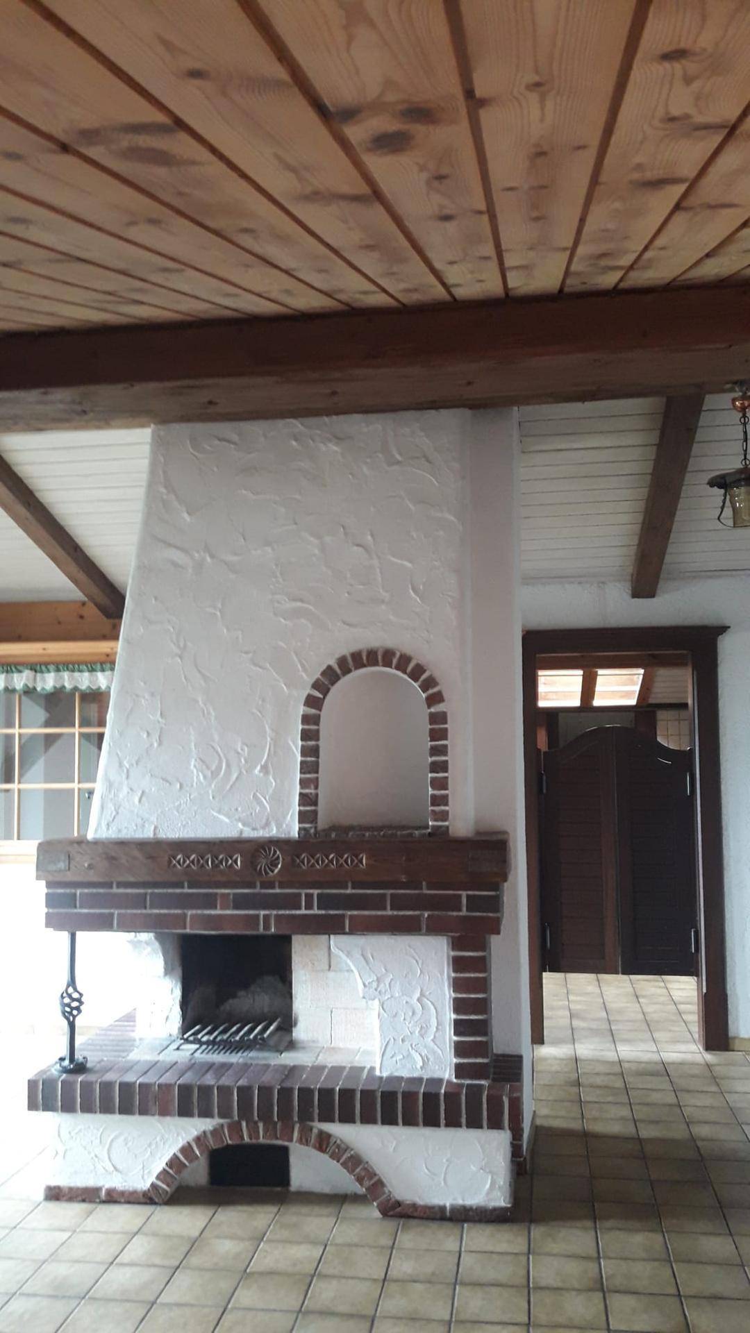 Rustikaler Wohnbereich mit gemauertem Kamin, Fliesenboden und Holzbalkendecke.