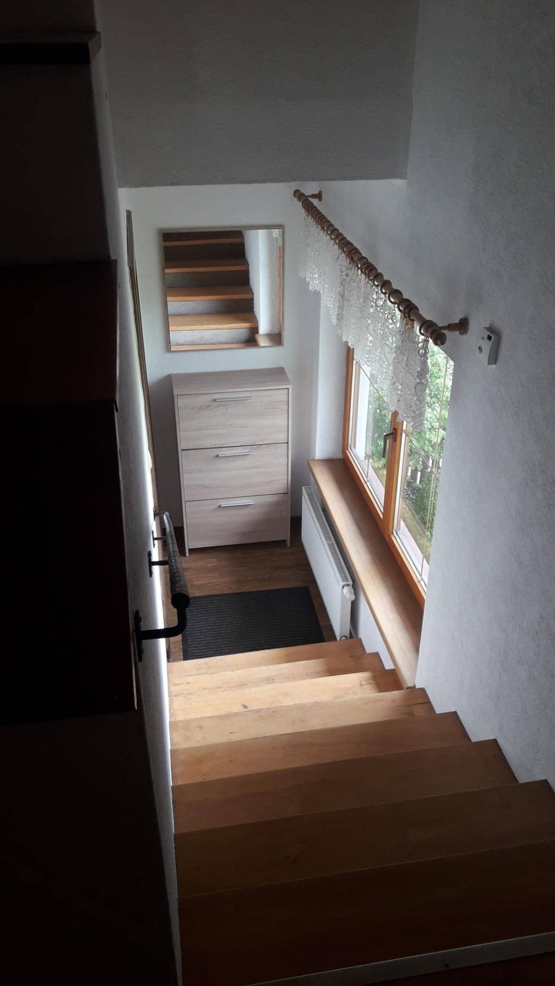 Holztreppe mit natürlichem Lichteinfall durch ein großes Fenster und einem kleinen Schrank.
