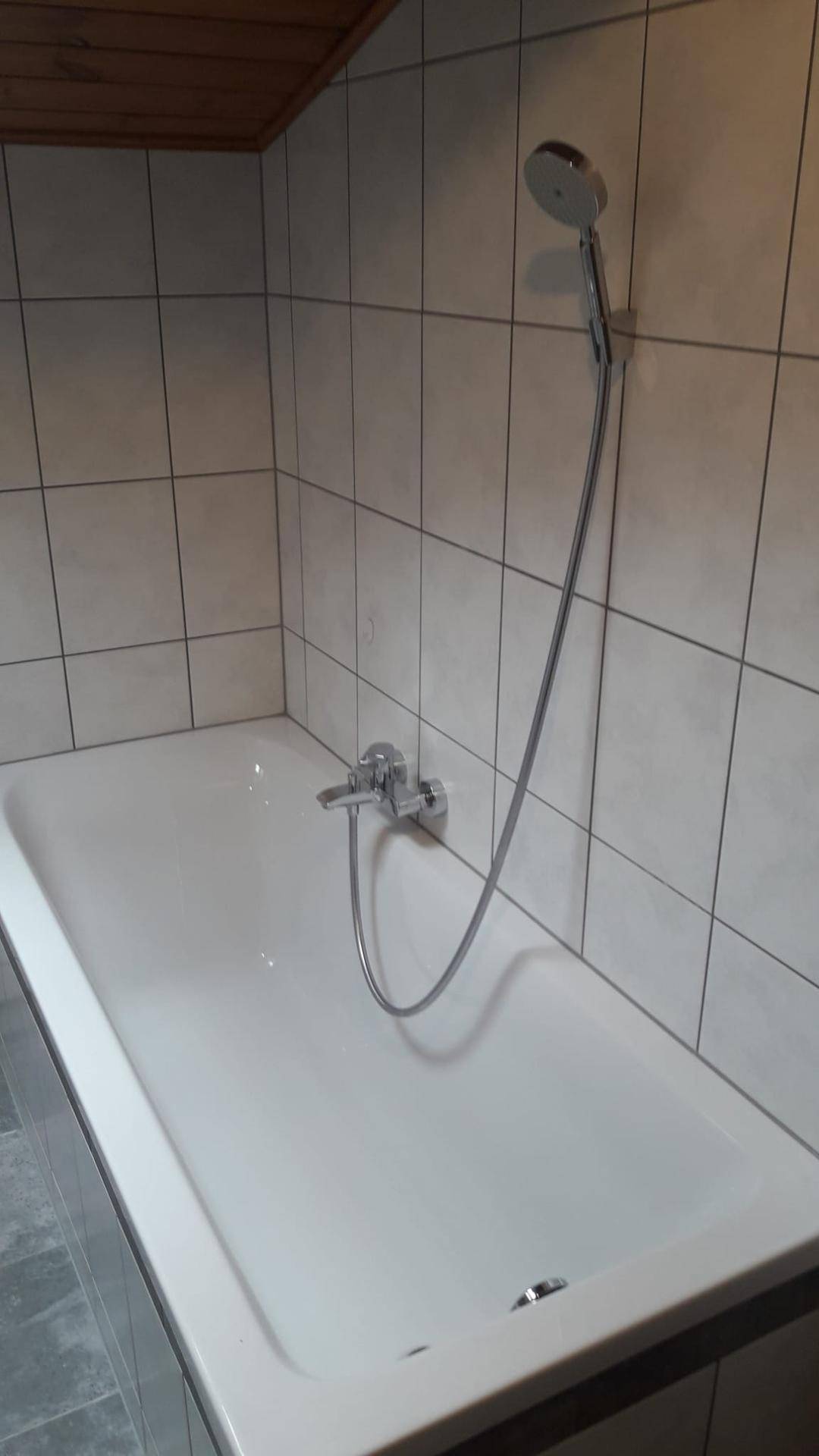 Badewanne mit Duschfunktion in einem gefliesten Badezimmer mit Holzdecke.