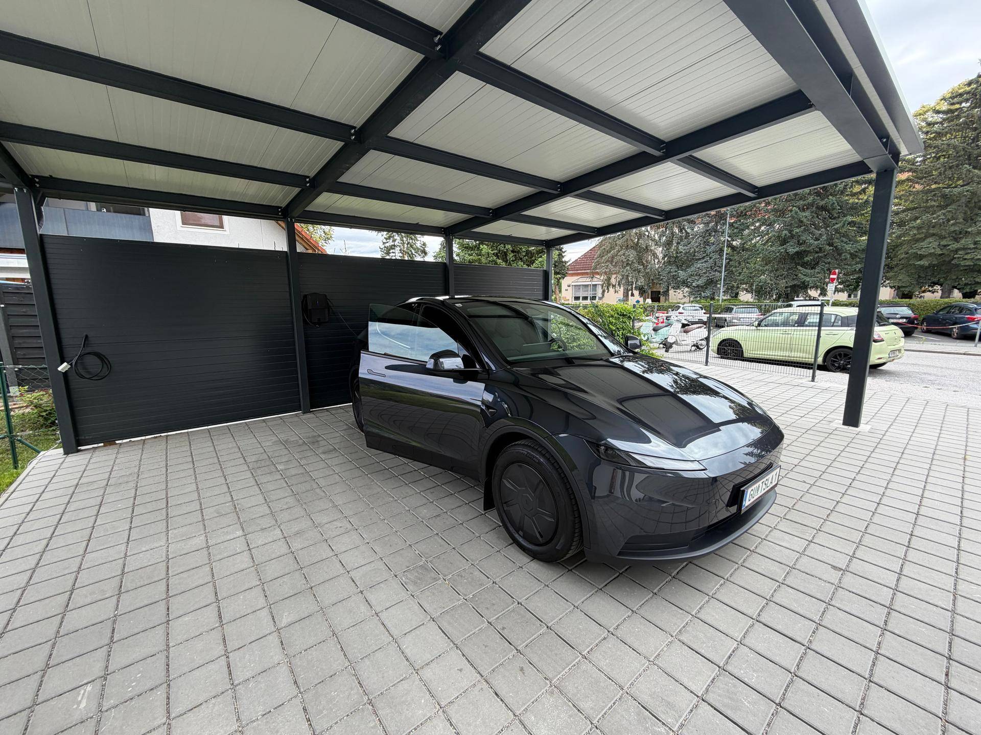 Modernes Carport mit gepflastertem Stellplatz und Elektrofahrzeug-Ladestation.