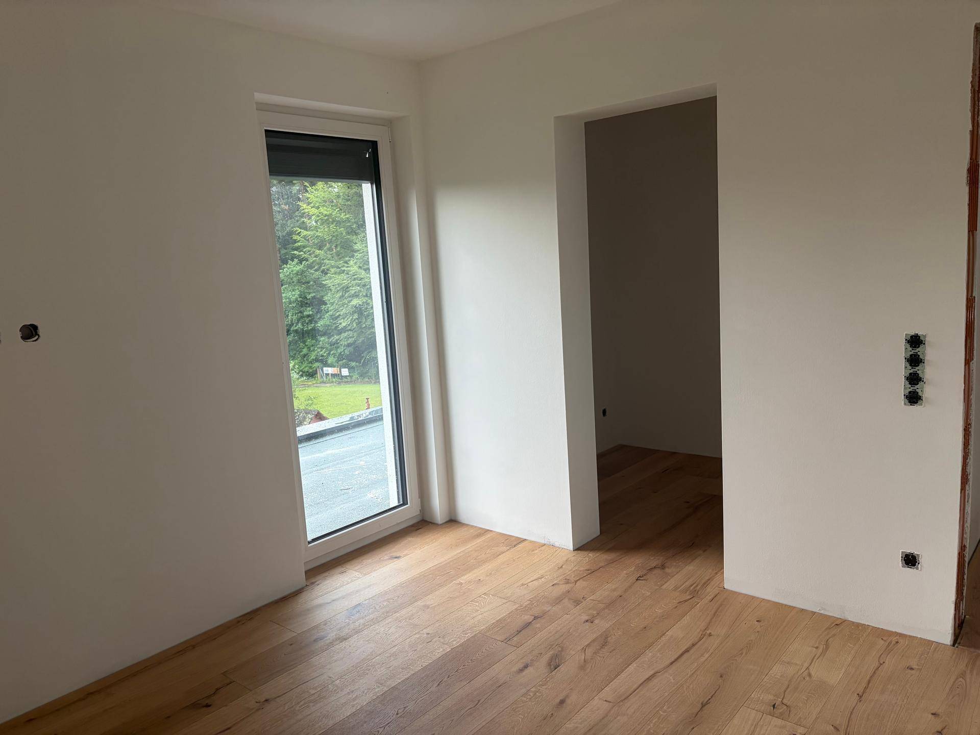 Heller Raum mit Holzboden und Zugang zu einem Außenbereich, noch unmöbliert.