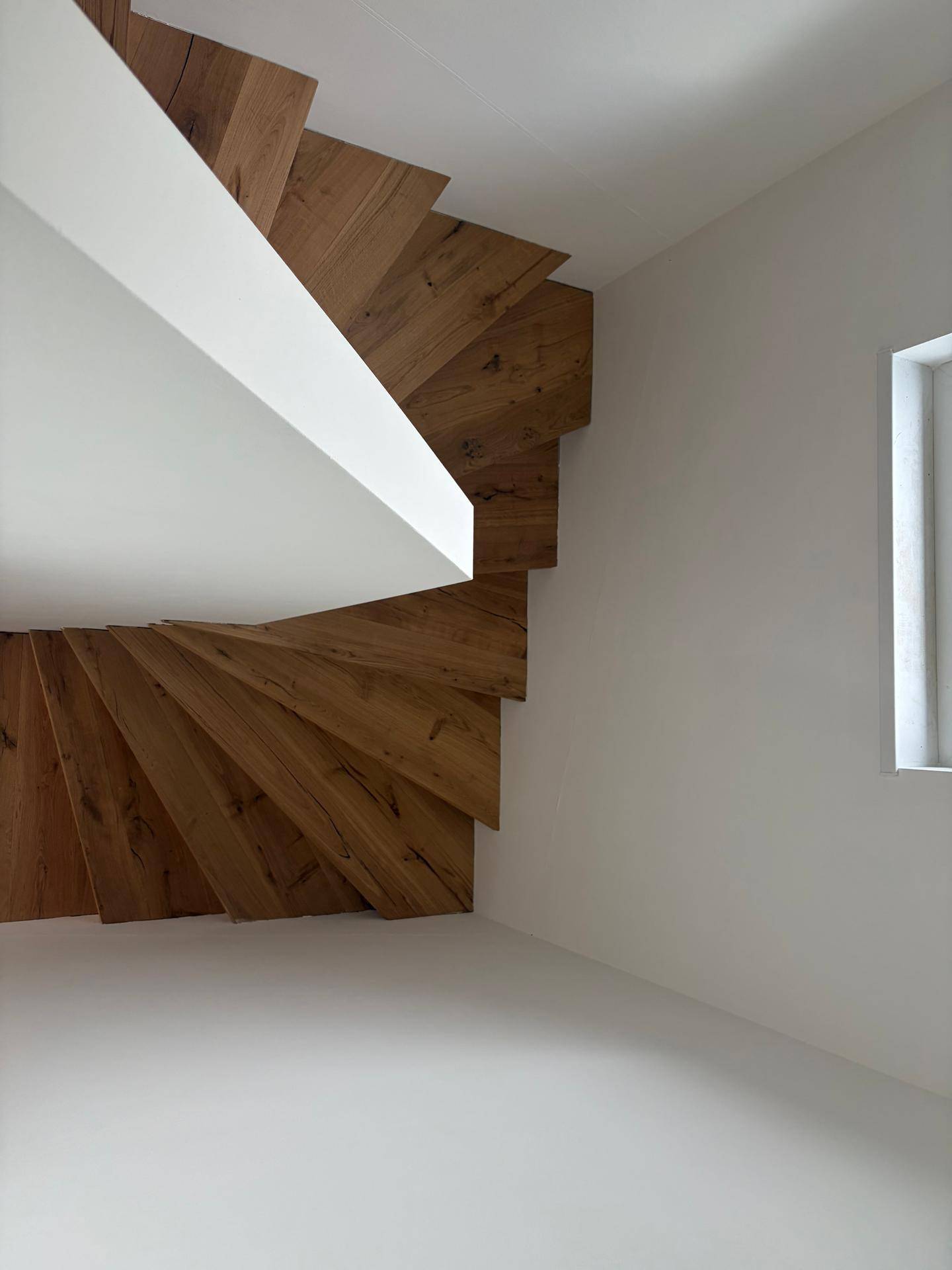 Moderne Holztreppe mit offenen Stufen und weiß gestrichenen Wänden.