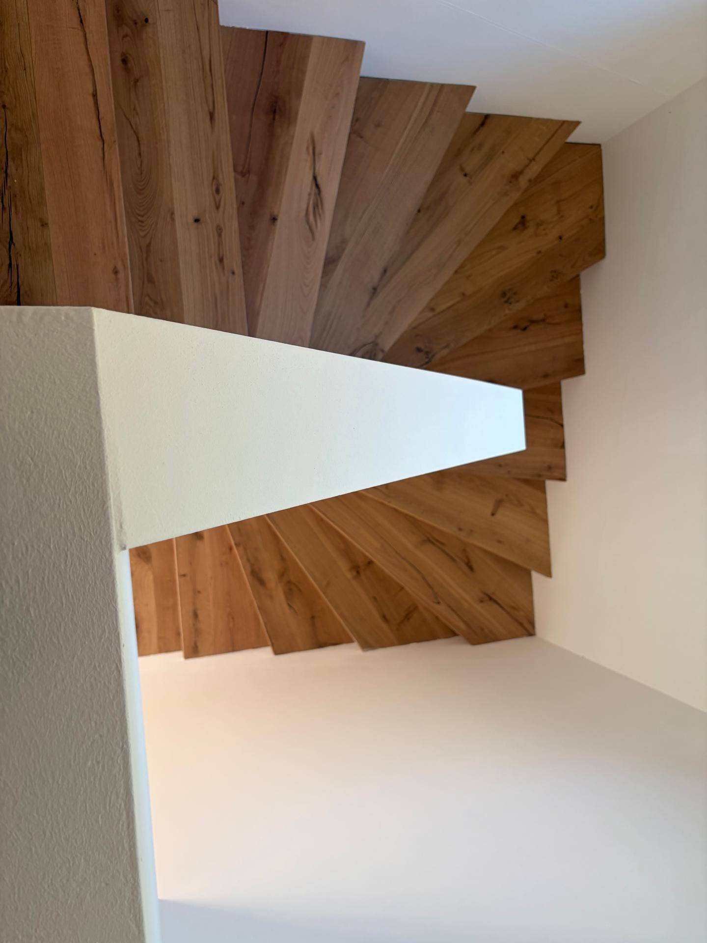 Moderne Holztreppe mit schwebenden Stufen und klaren Linien im Treppenhaus.