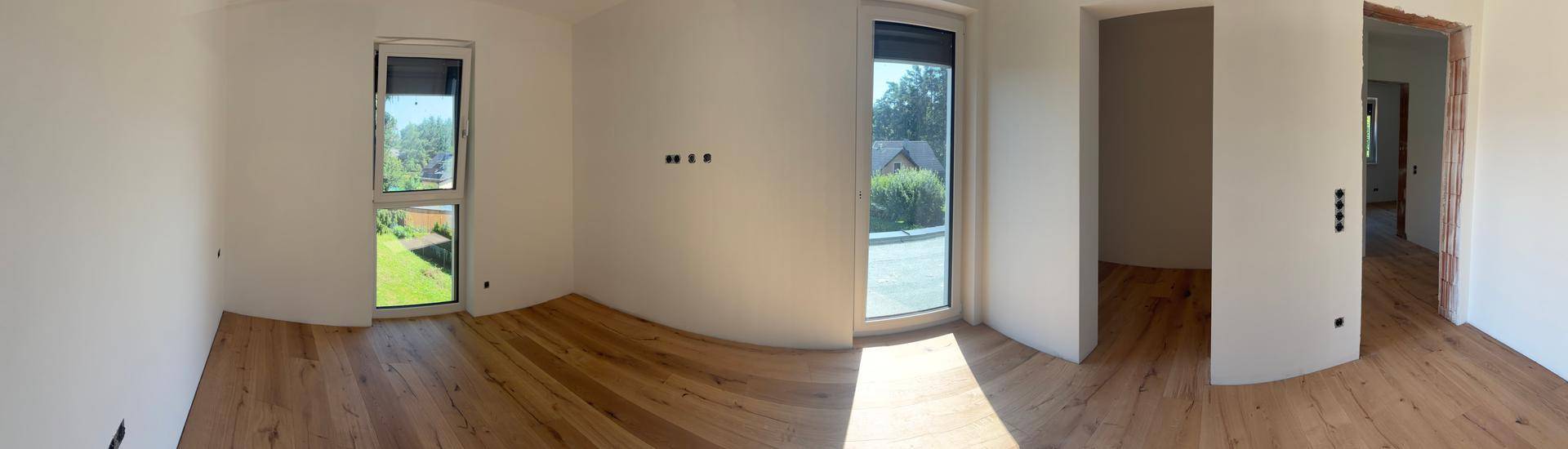 Weitläufiger Raum mit Holzboden und großen Fenstern, die viel Licht hereinlassen.