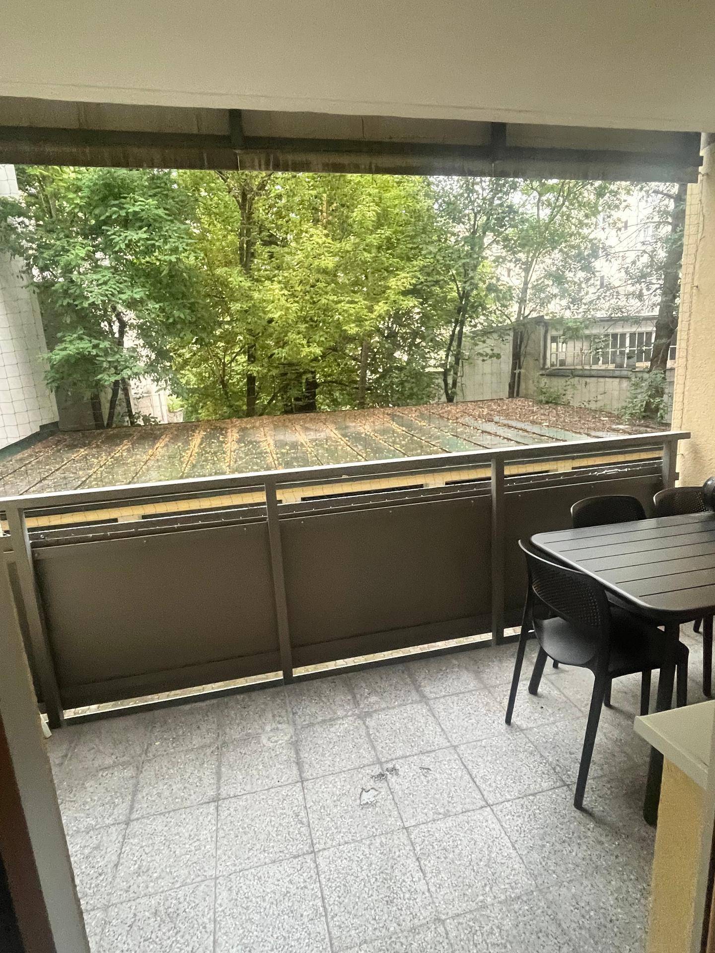 Überdachter Balkon mit Fliesenboden, Sitzgelegenheiten und Blick ins Grüne.