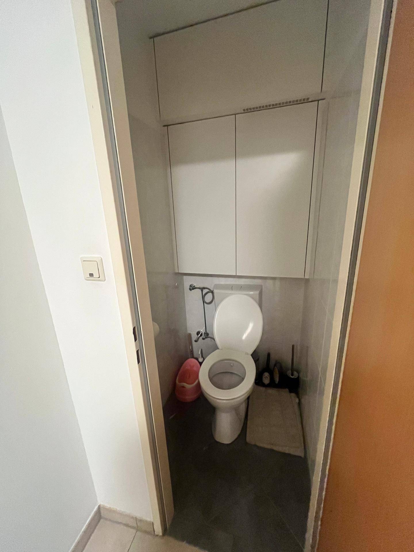 Separates WC mit Toilette, kleinen Schränken und dunklem Fliesenboden.