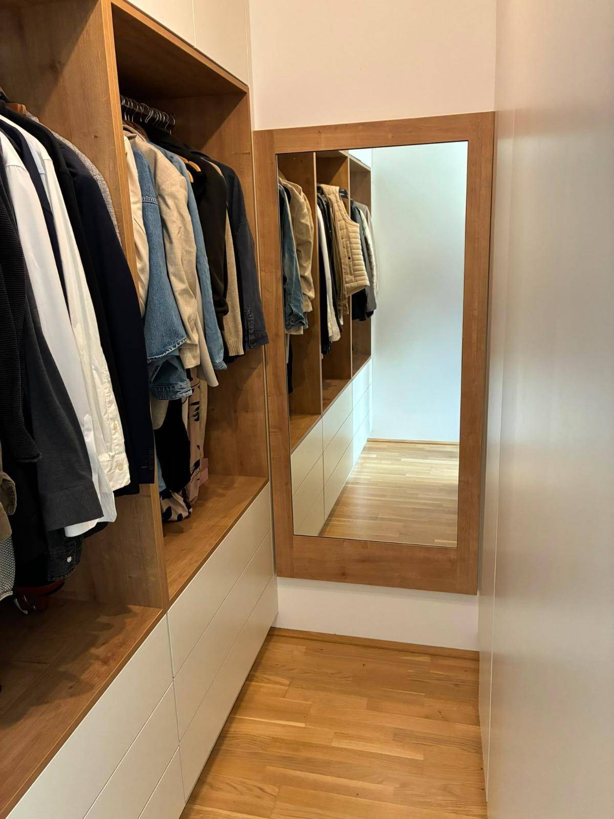 Geräumiger begehbarer Kleiderschrank mit Holzelementen und großem Spiegel.