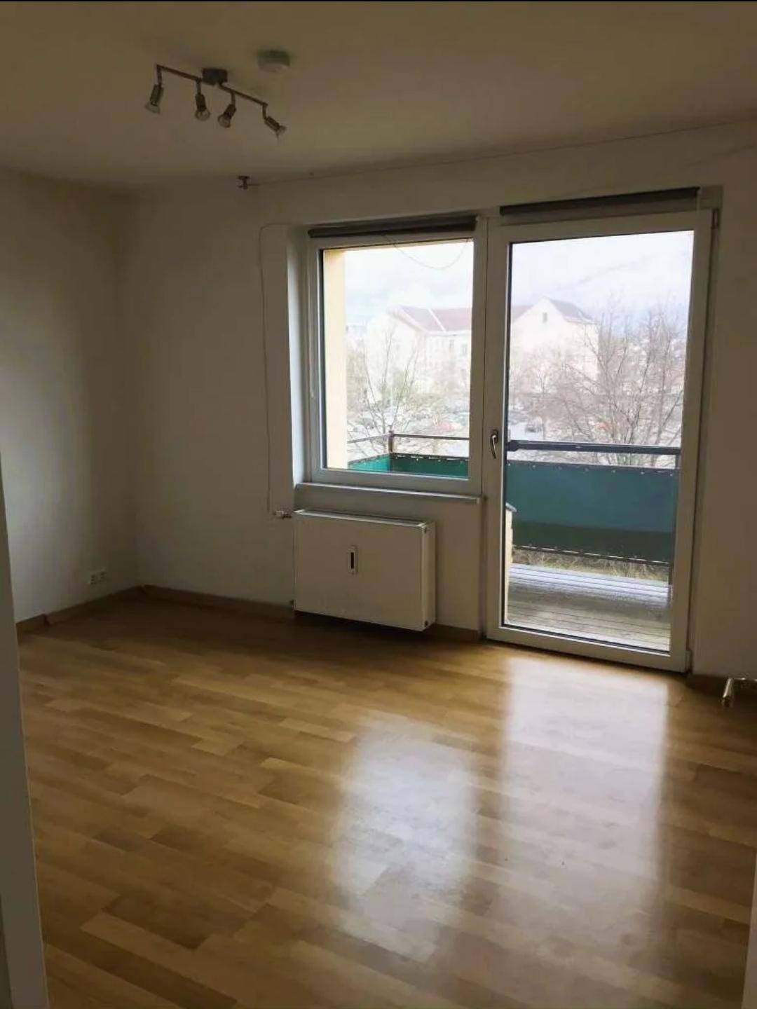 Lichtdurchflutetes Zimmer mit Holzboden und Zugang zu einem Balkon, ideal als Schlafzimmer.
