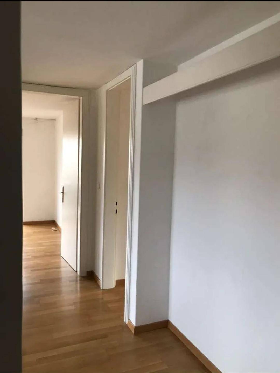Heller Flur mit Holzboden und weißen Wänden, der zu weiteren Räumen führt.