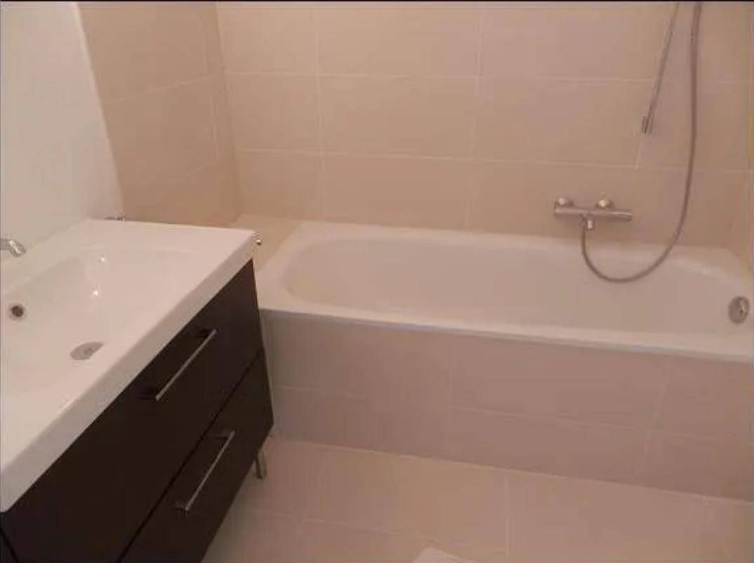 Badezimmer mit einer sauberen Badewanne und hellen Fliesen an Wänden und Boden.