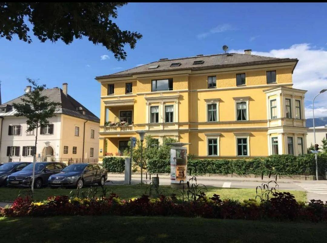 Historisches gelbes Gebäude mit klassischer Architektur und gepflegter Grünanlage im Vordergrund.