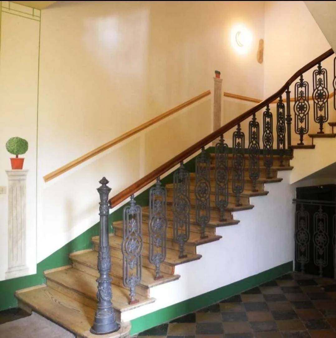 Elegantes Treppenhaus mit kunstvollen Metallgeländern und Holzstufen, das den Charme des Gebäudes unterstreicht.